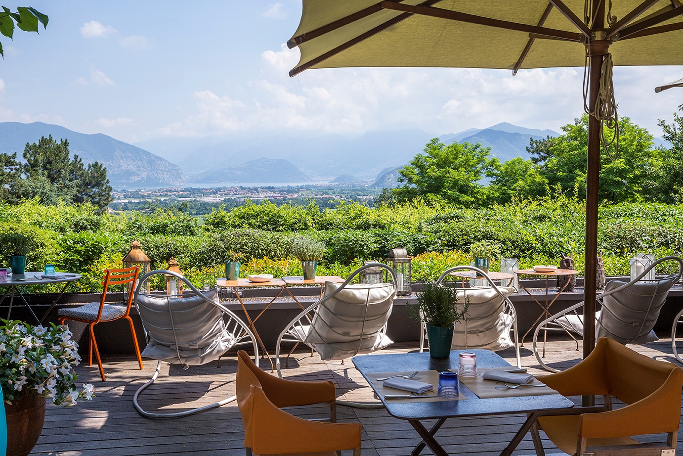 A terrace with tables, chairs and umbrellas overlooking a green vineyard and mountains in the distance.
