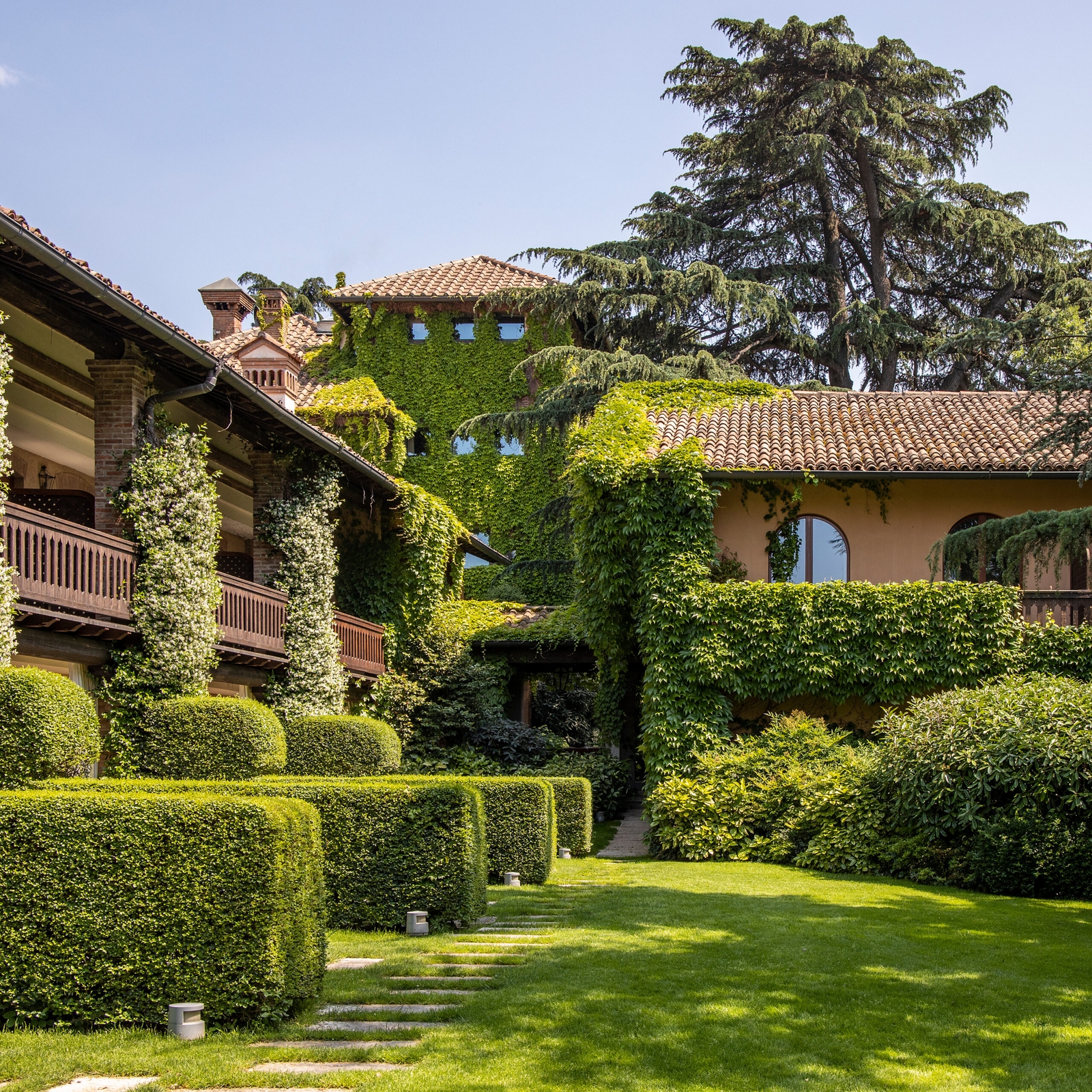 Exterior of a villa covered in ivy with lots of hedges and green lawns.