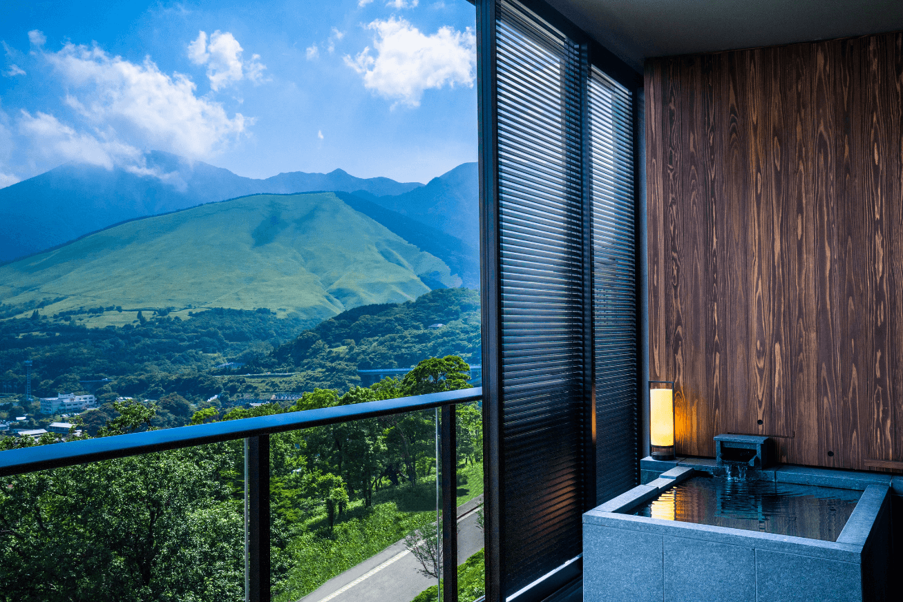 A balcony with a small private onsen and a view of green mountains and blue sky