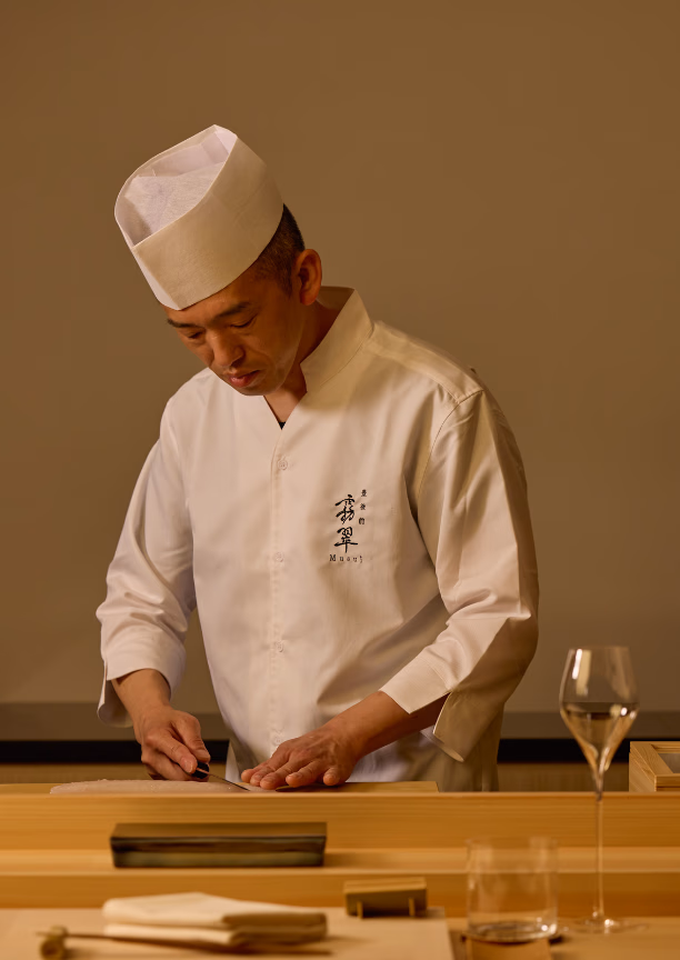 A man in a white chef's coat and hat slicing fish