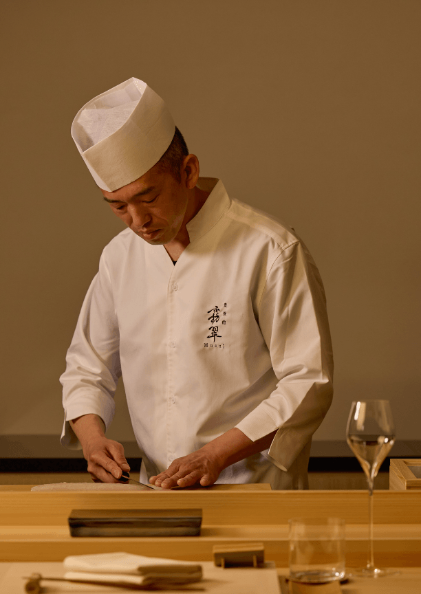 A man in a white chef's coat and hat slicing fish