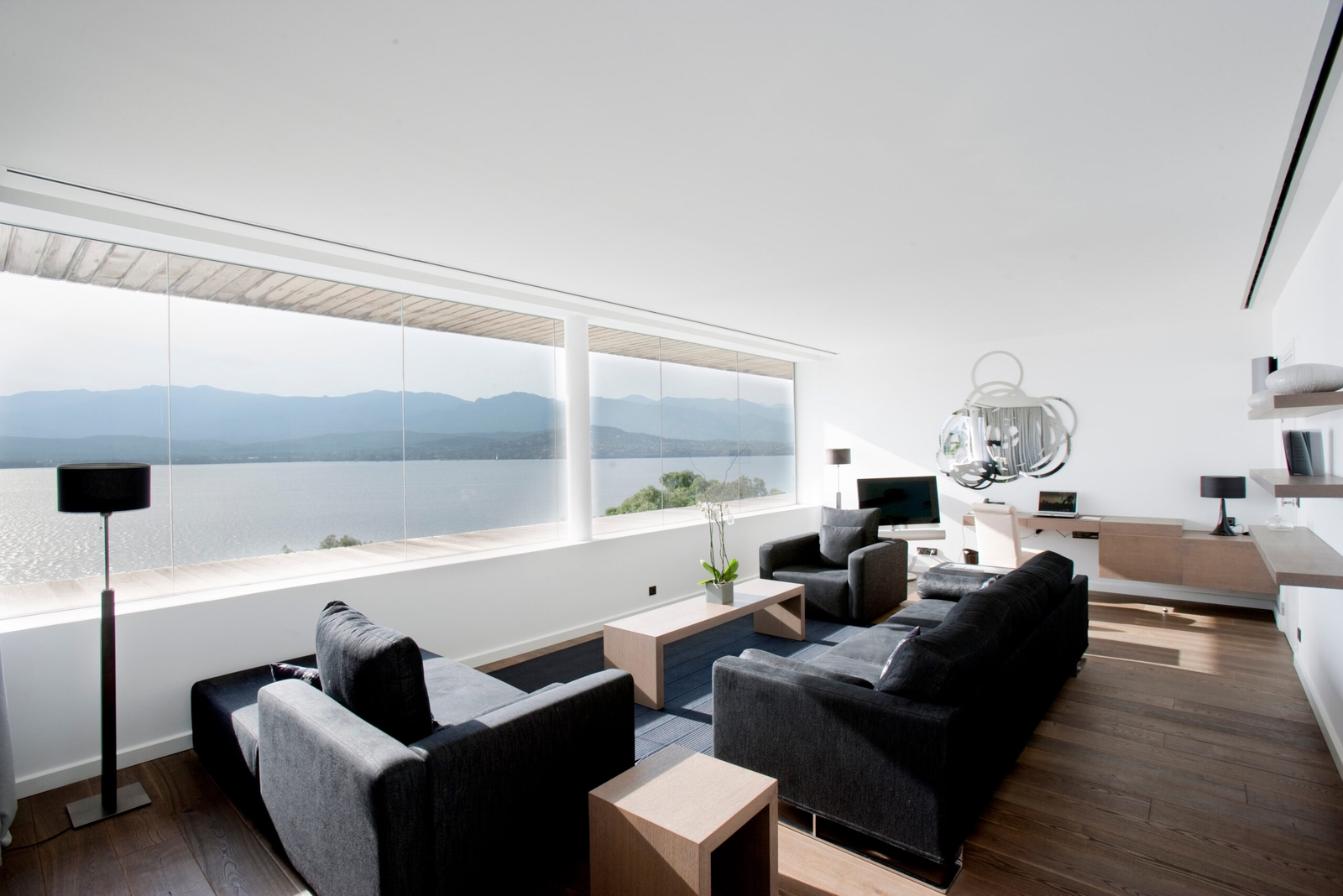 Interior of a suite living area with black sofas and white walls, and a long picture window overlooking the sea.