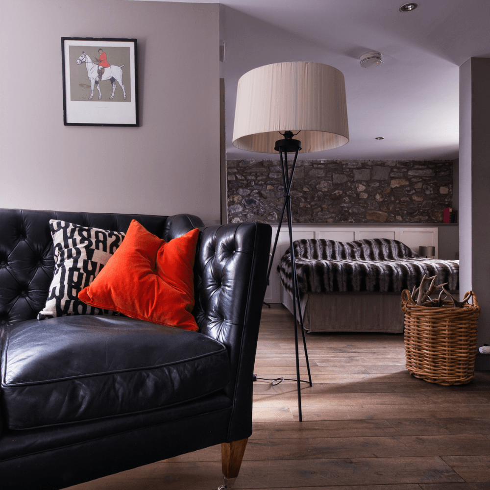 Modern hotel room with a black leather sofa, red throw pillow and bed in the background