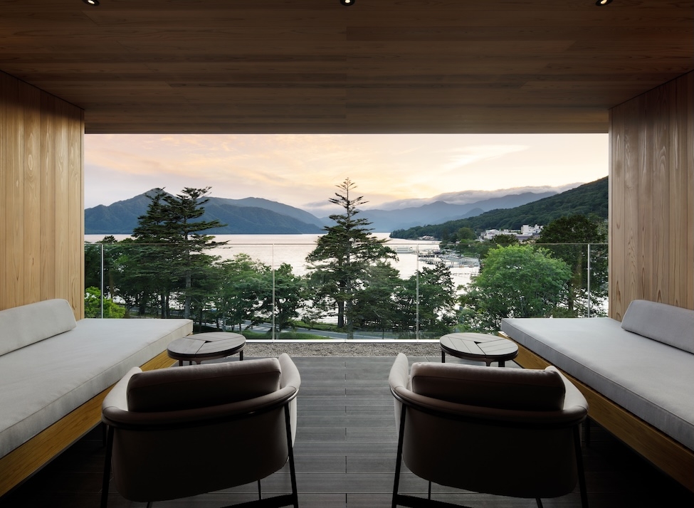 Sunset view of lake and mountains from balcony with two chairs and sofas