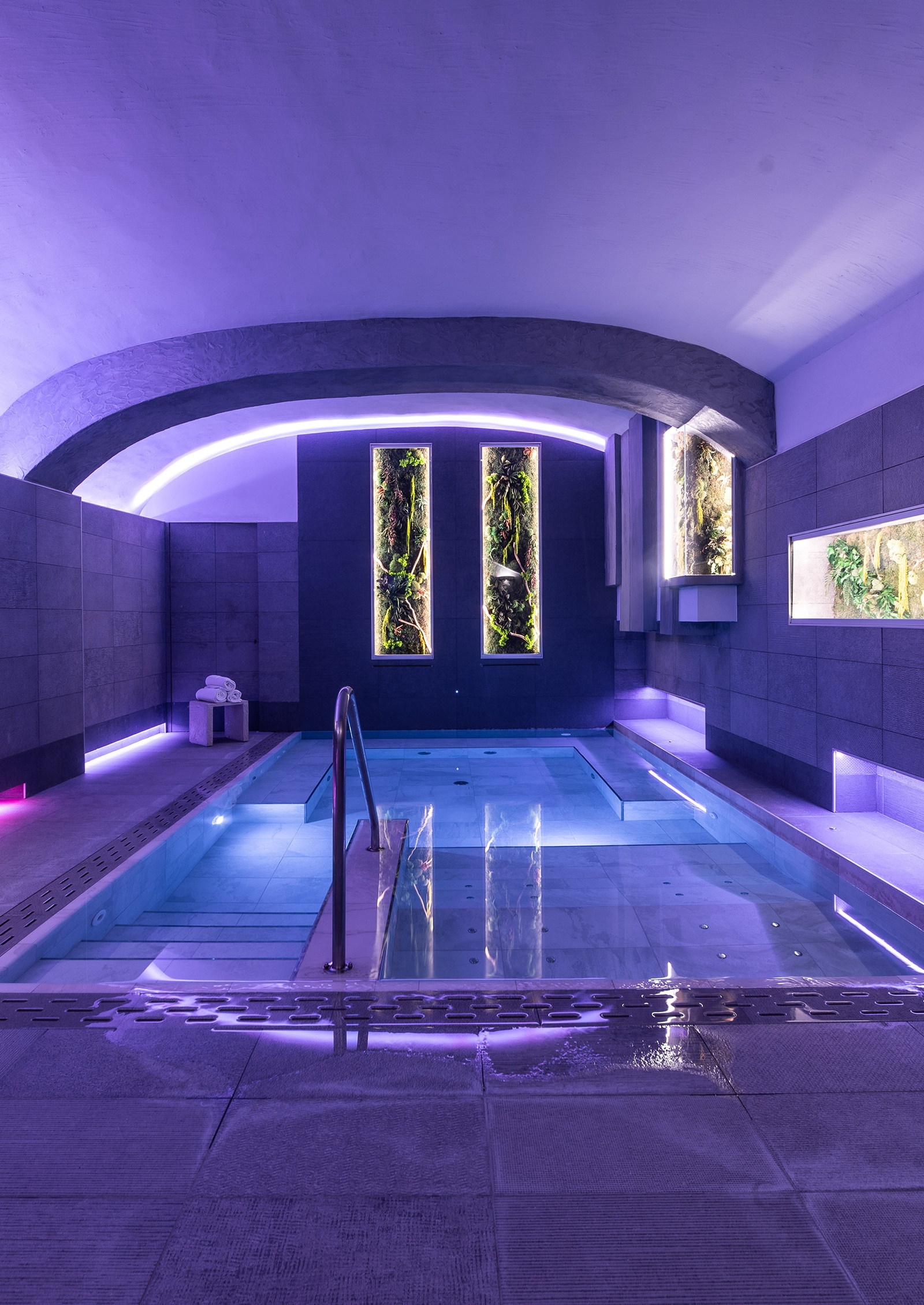 Indoor pool with purple lighting and two long windows at the back of the room.