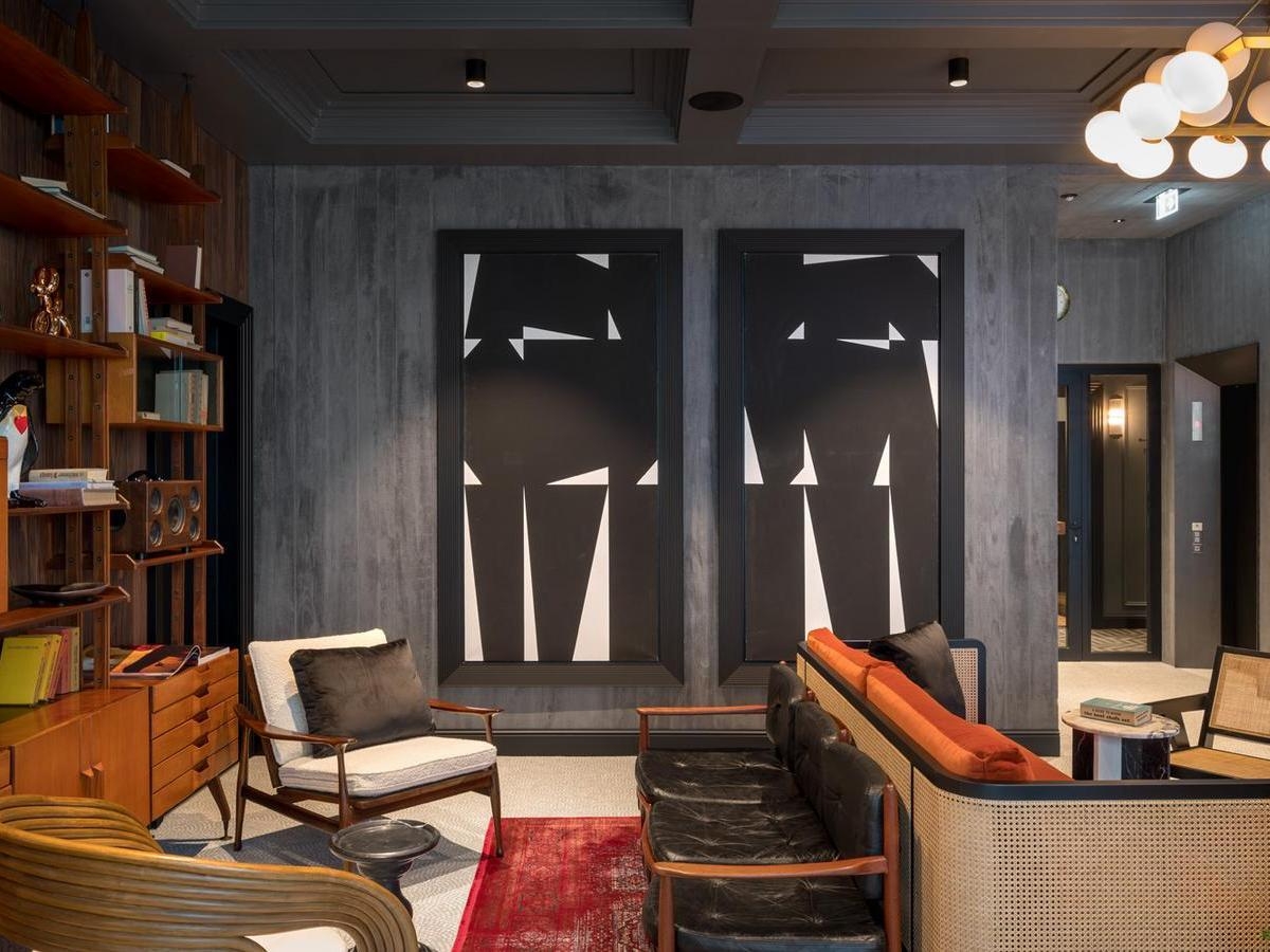 Chic hotel lobby with black and white abstract paintings, vintage-style seating, and a red patterned rug.