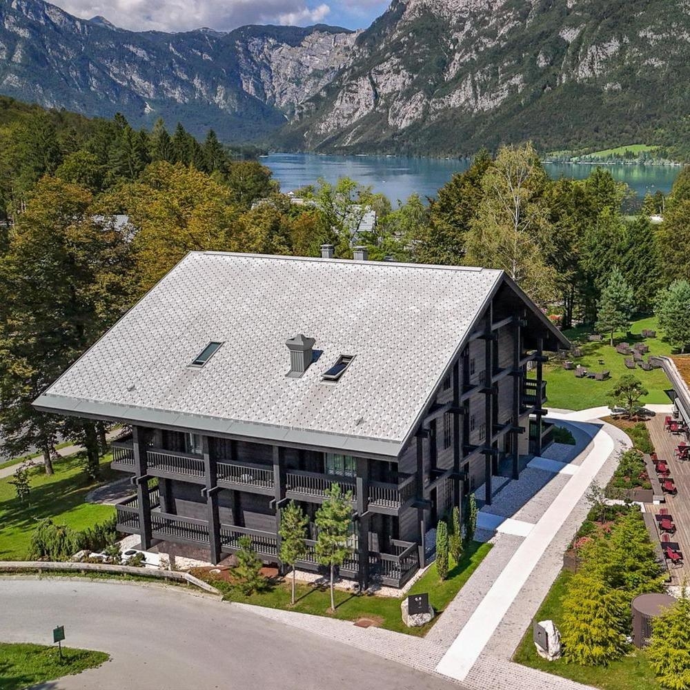 High-angle view of a dark wood chalet with a grey roof and a modern building with a grass-covered roof.