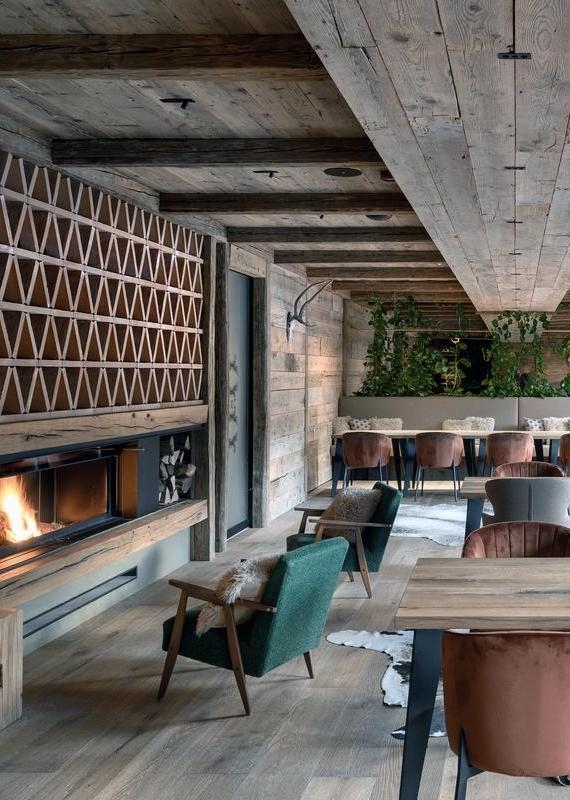 Restaurant dining room with wooden beams, a fireplace, and velvet chairs arranged along a wood-paneled wall.