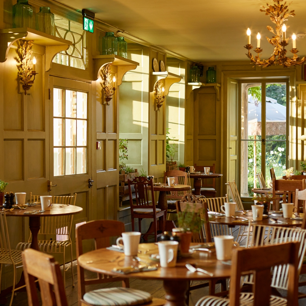Interior of a restaurant dining room with light wood tables and warm chandeliers and wooden walls.