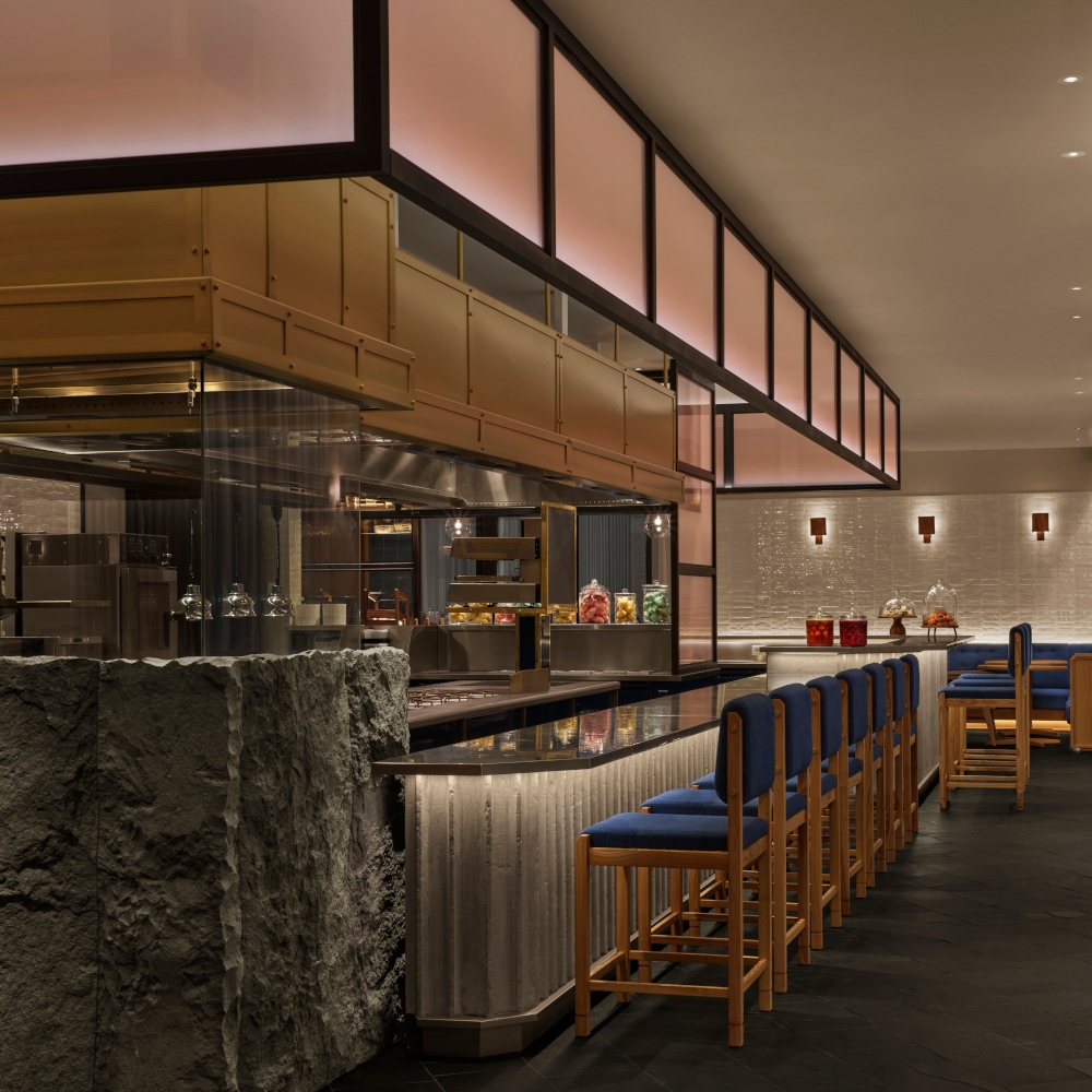 Interior of a restaurant's bar seating with chairs with blue cushions along a grey stone bar seating area.