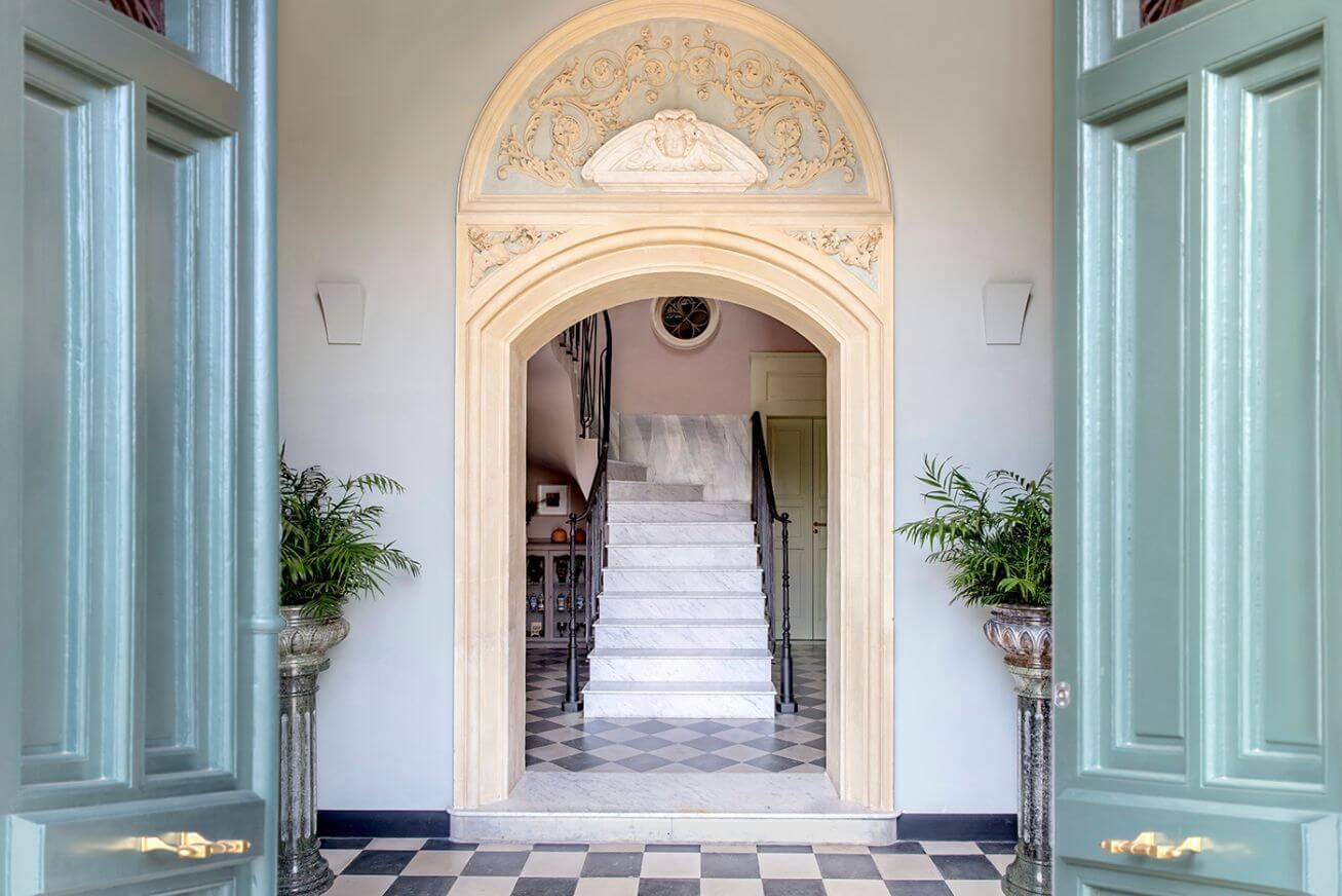 An entryway with a tiled floor, ornate arched doorway, marble staircase and turquoise double doors
