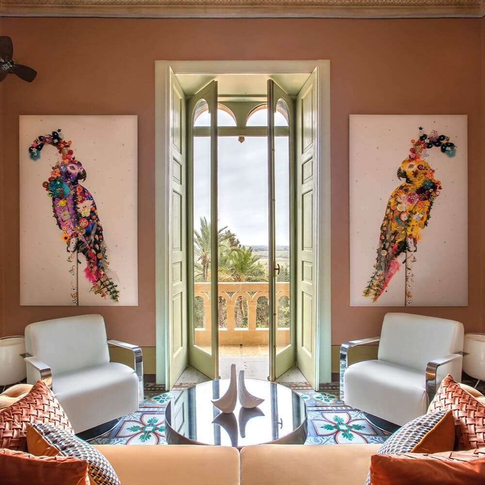 A living room with doors open to a sunny balcony and two colourful paintings of birds on either side