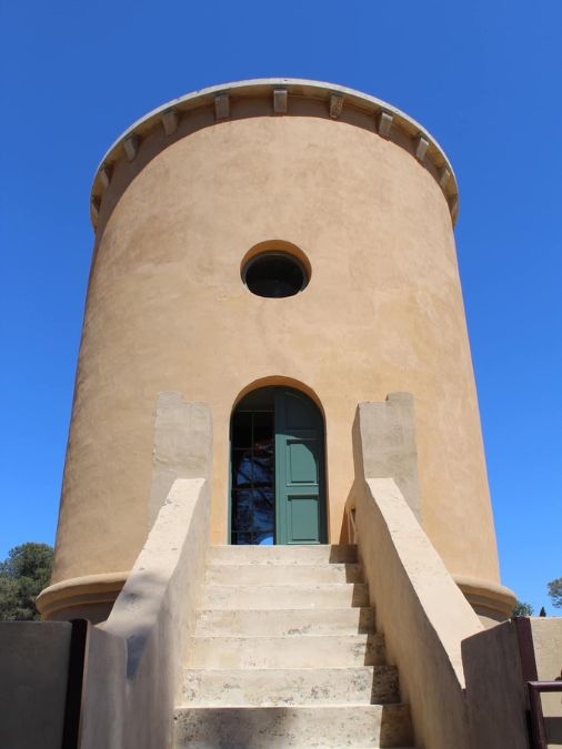 A smooth stone tower with an arched doorway and stairs leading up to it