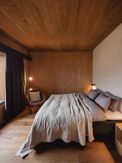 A large bed in a warmly lit room with wooden walls, floor and ceiling.