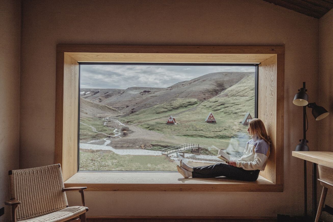 A large picture window with mountain views and a woman reading on a window seat.
