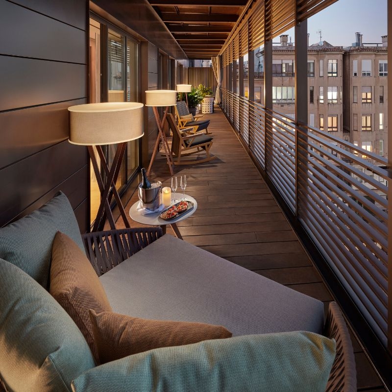 A long wooden balcony with several chairs, lamps and a small table set with sparkling wine and a plate of food