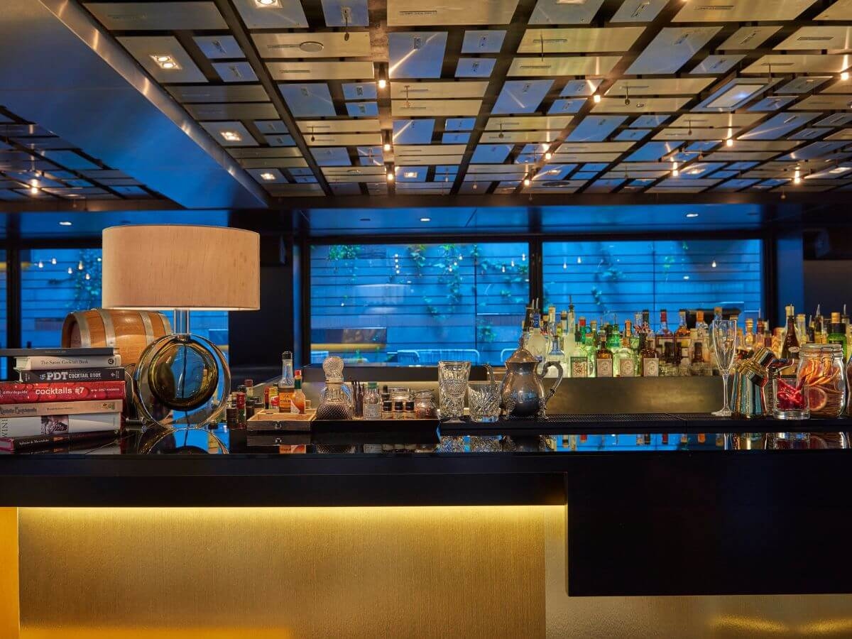 A hotel bar with drinkware, bottles, books and a lamp