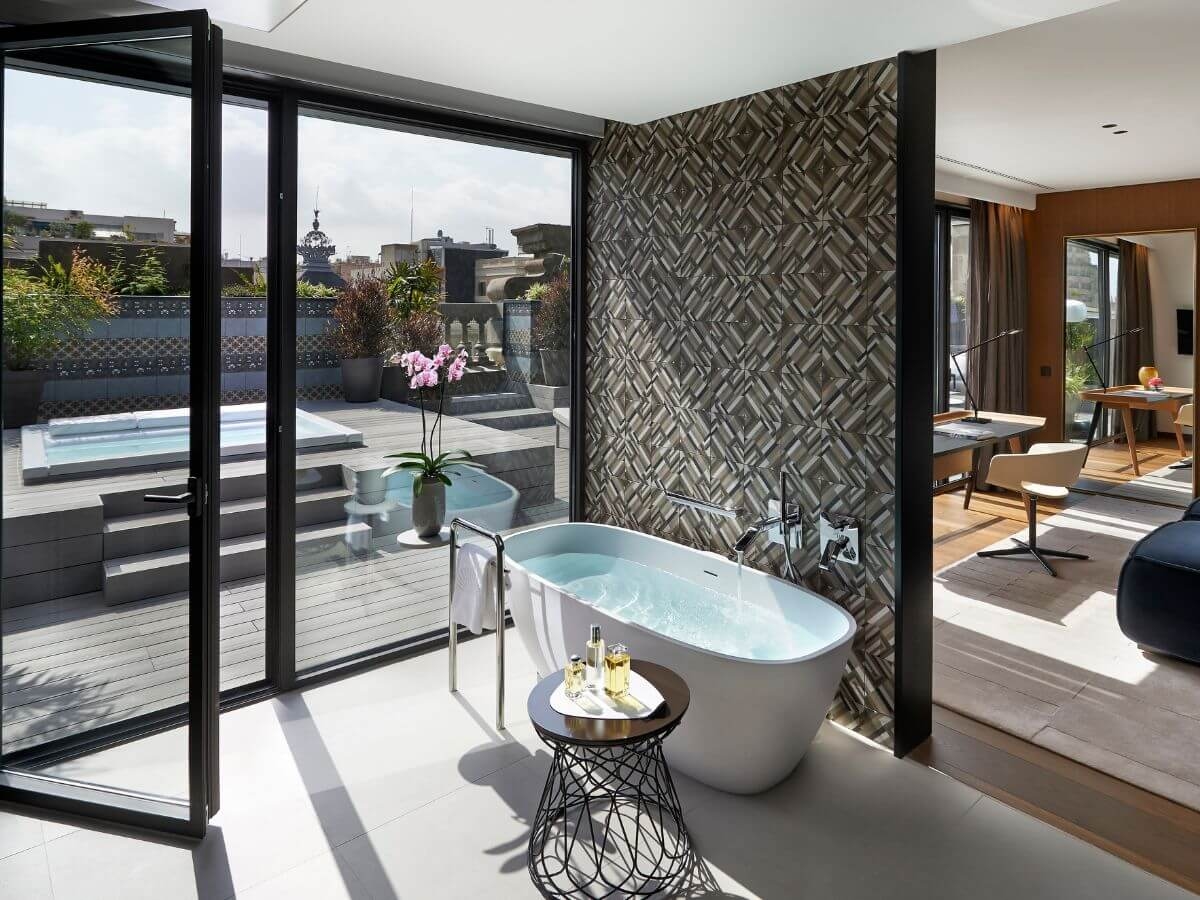 A hotel bathroom with a freestanding tub and a door open to a terrace with a plunge pool