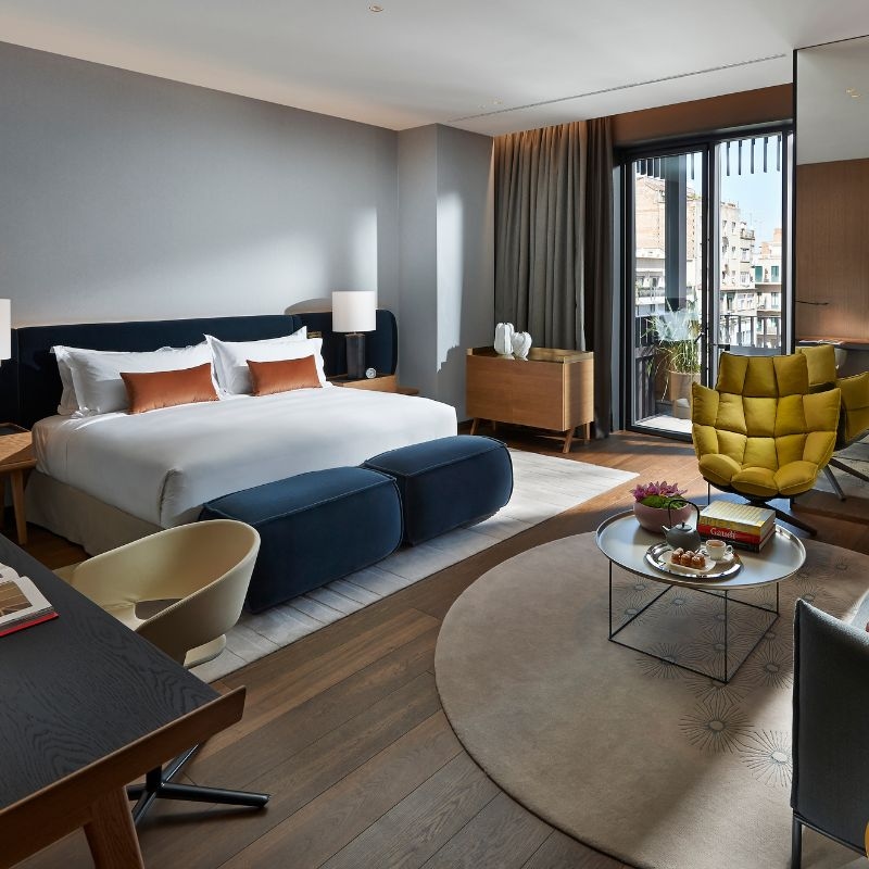 A hotel bedroom with a large bed, sitting area and double doors leading to a balcony