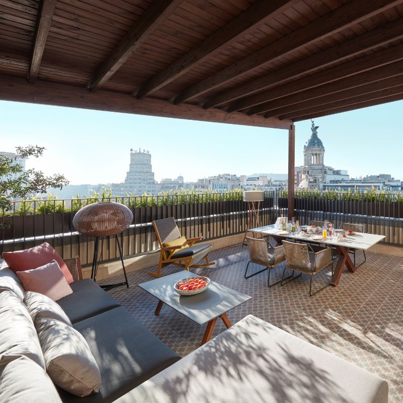 A large private terrace with a sofa, dining table, rocking chair and panoramic views of Barcelona