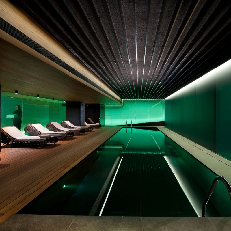 An indoor pool illuminated with green light, with several lounge chairs beside it