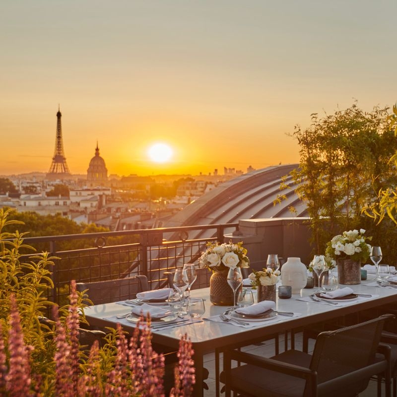 A sunset view of the Eiffel Tower from a rooftop terrace with a table set for eight