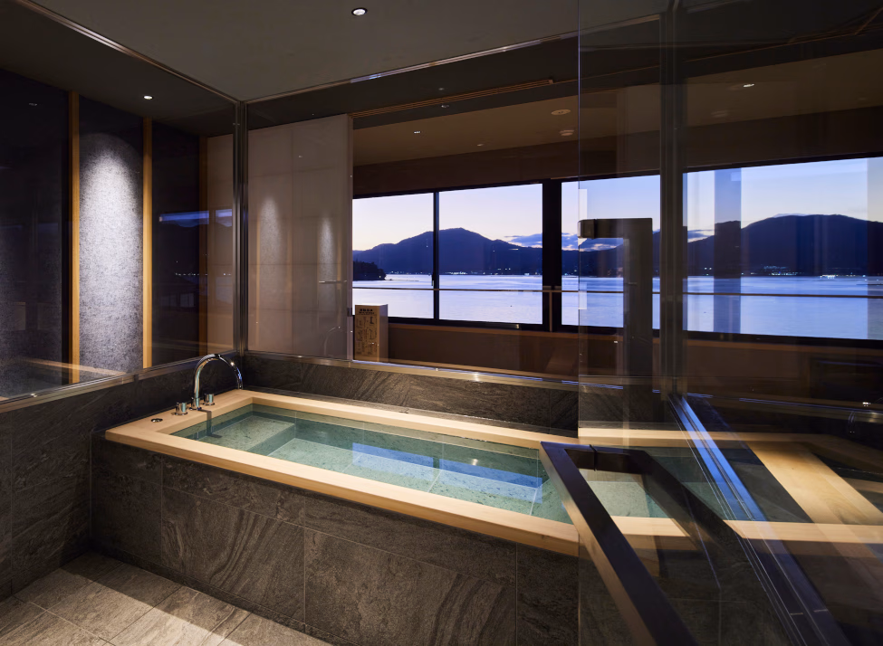 Interior of a corner bath with dual-aspect windows overlooking the sea and mountains with a purple sunset.
