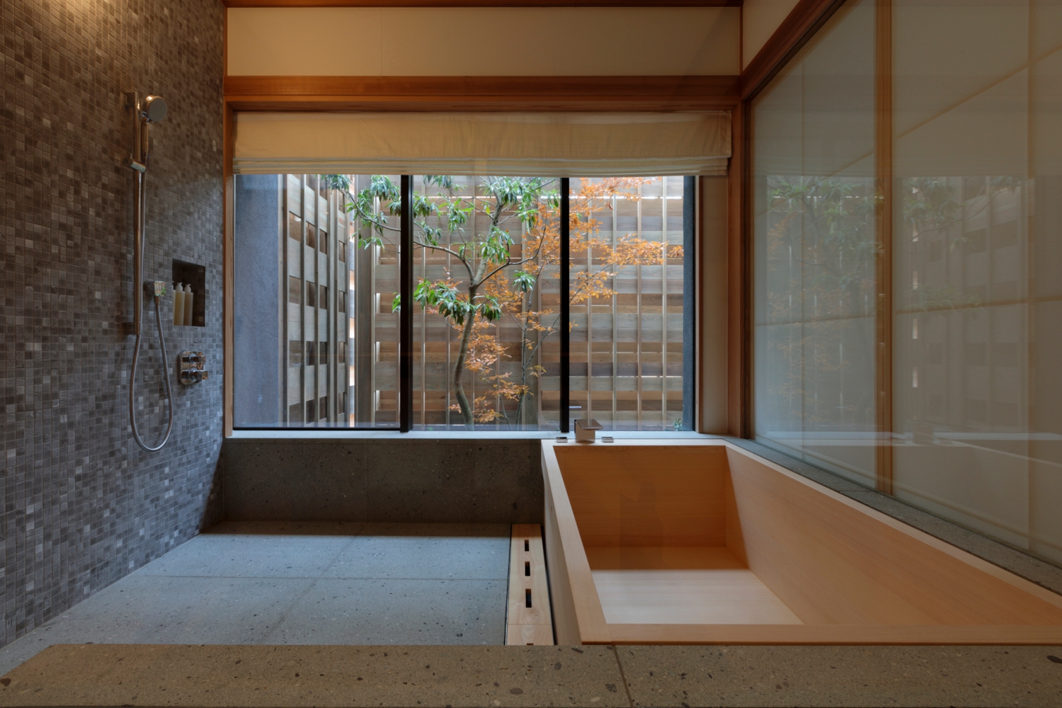 Interior of a simple bathroom with a deep, cedar bathtub, stone shower and large picture windows overlooking an outdoor Zen garden.