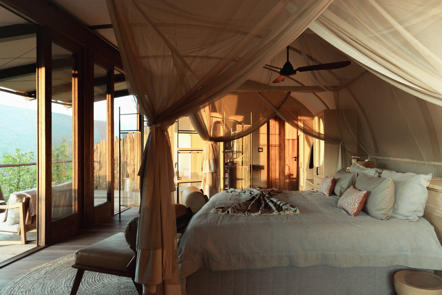 Interior of a safari suite bedroom with a bed with white bedding and a beige mosquito net, and large windows opening onto a deck overlooking a valley.