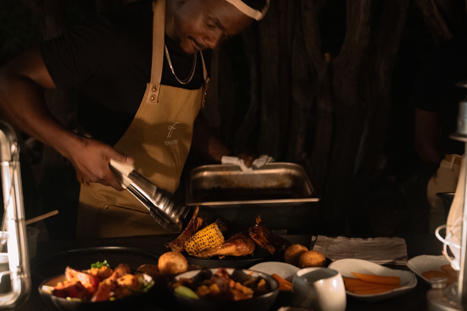 A person wearing an apron places food onto places in a darkened kitchen.