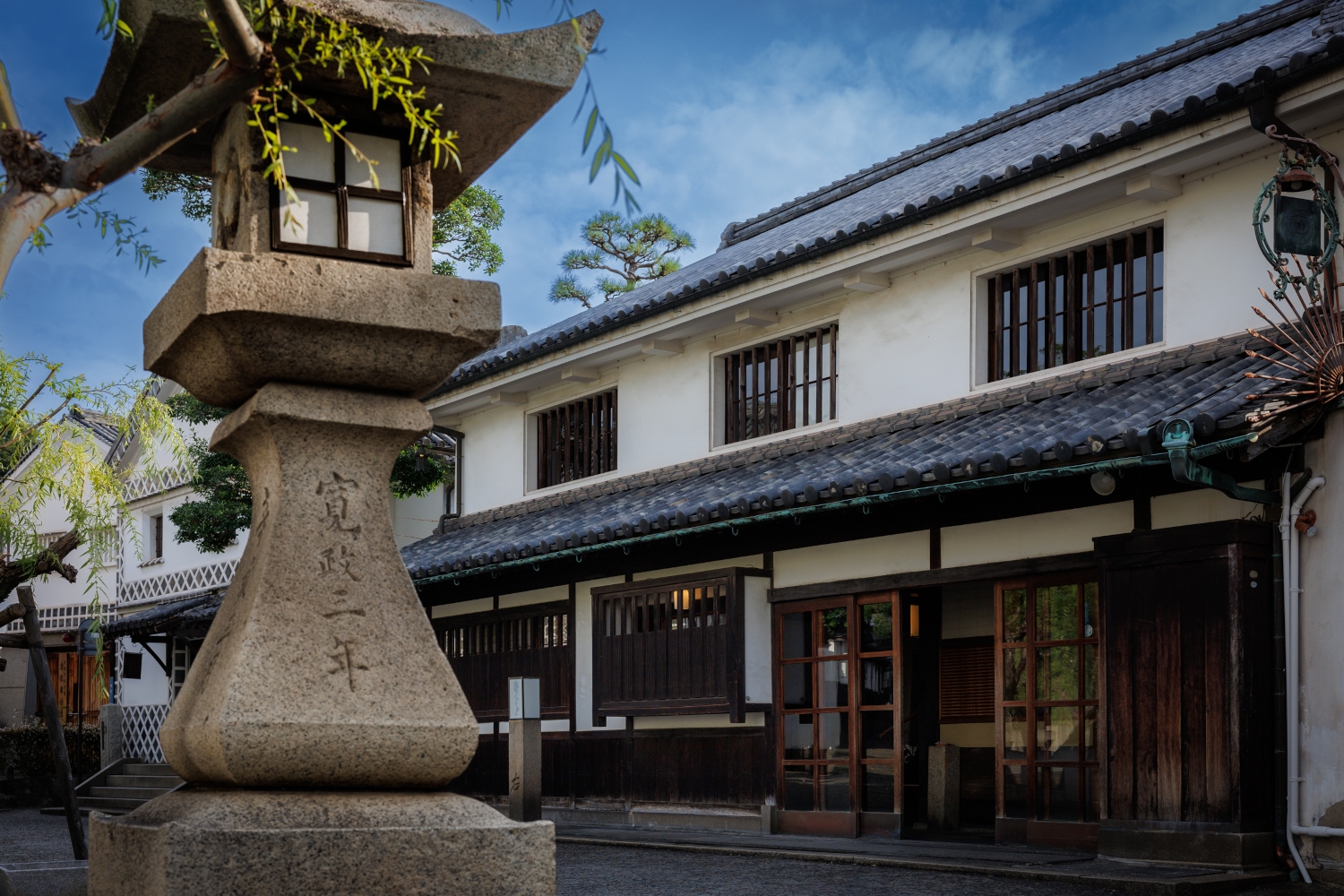 Exterior of the historic tile-roofed ryokan with a small stone shrine in the foreground.