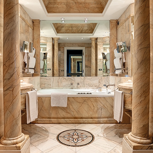 A marble bathroom in a hotel room with off-white columns, a large mirror, bath tub and white towels.