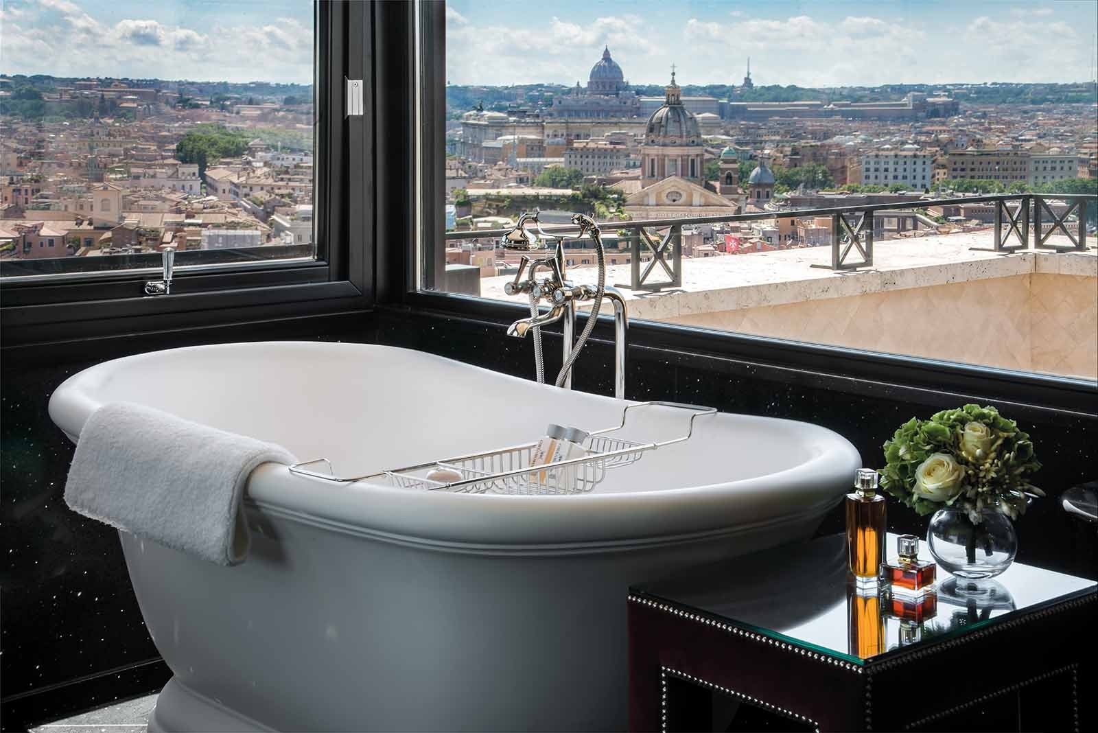 A large bath tub in a presidential suite with black-framed windows that look out to a terrace and rooftops in central Rome.