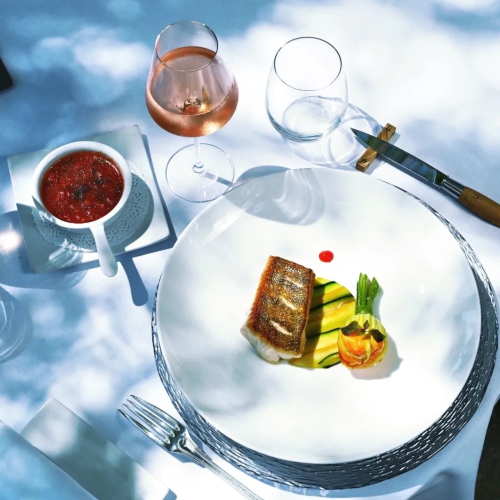 Overhead view of a plate of delicately presented food on a white plate with two glasses of wine and a bowl of soup on the side.