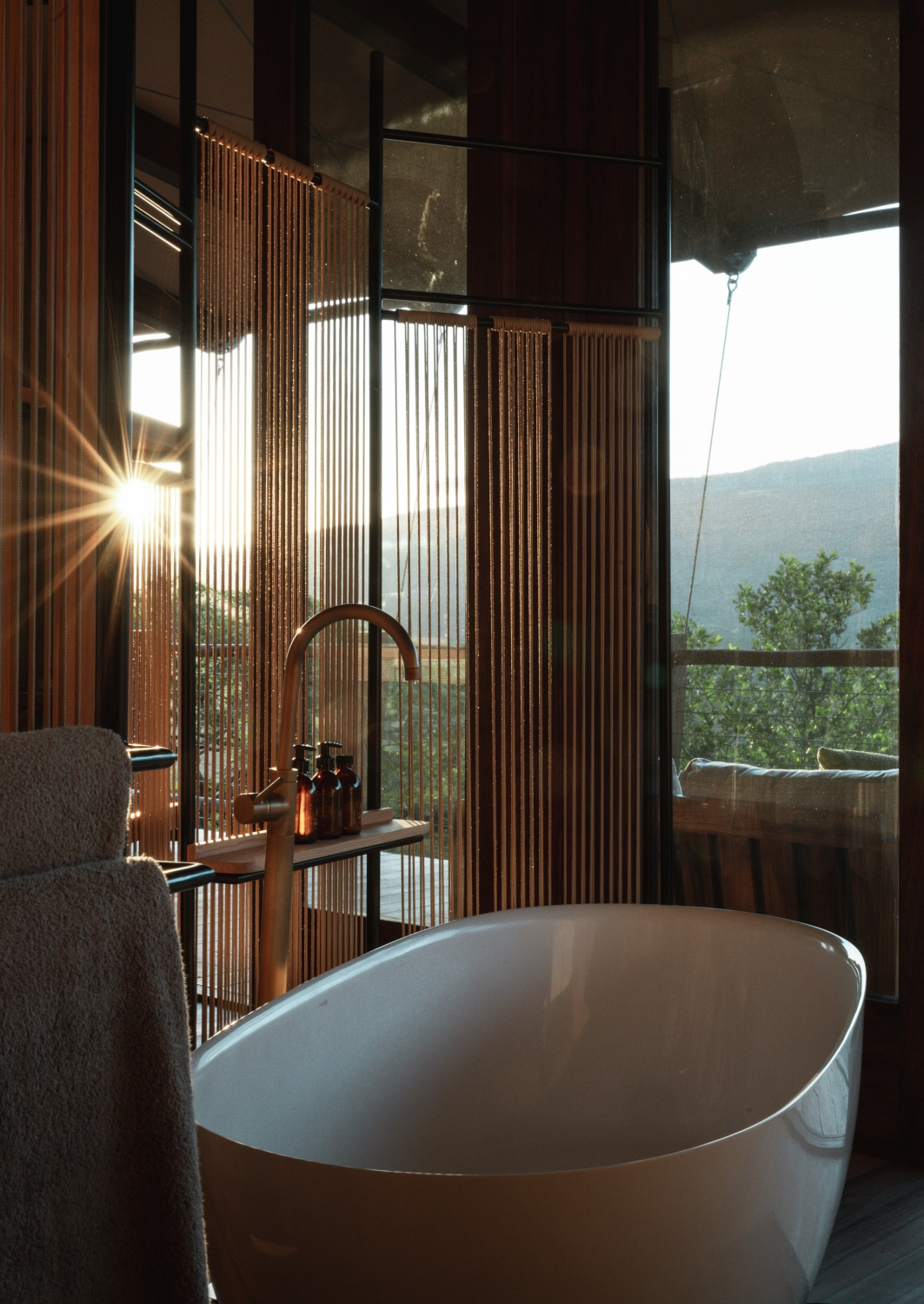 Interior shot of a white oval deep standalone bathtub facing out onto large windows overlooking a sunset and mountains.
