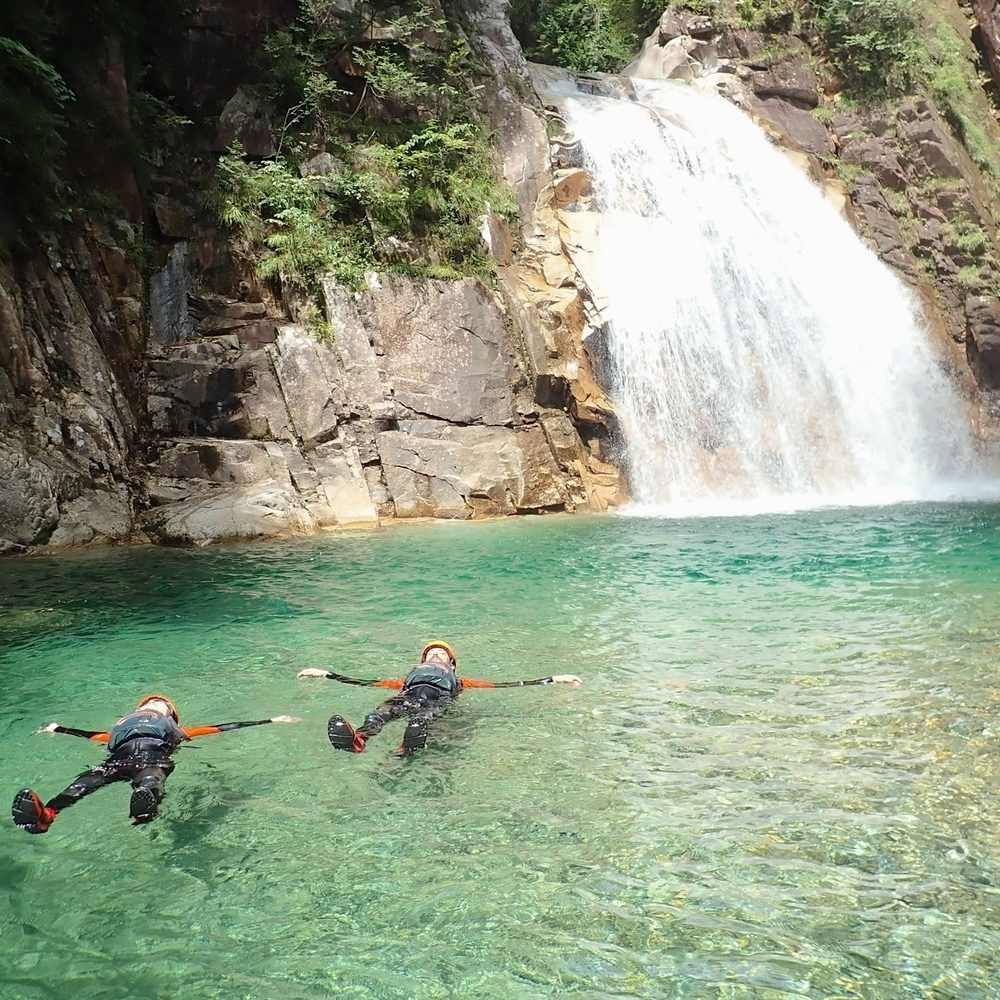 Two people floating in a clear pool by a waterfall