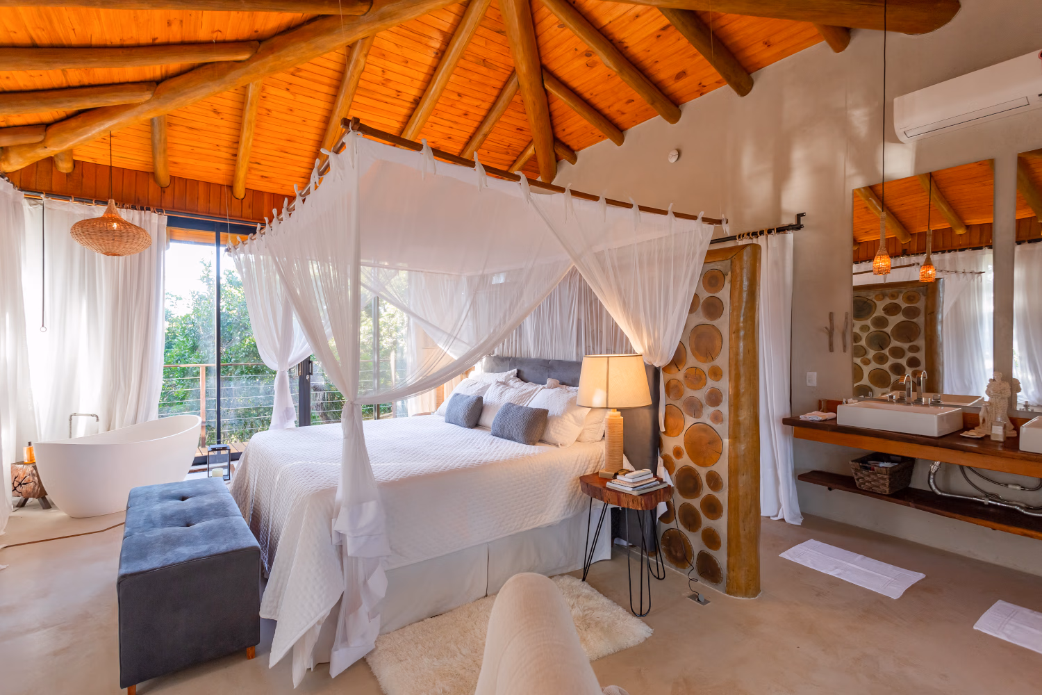 Bonito Villa bedroom with canopy bed with white bedding, a pitched wooden ceiling and large glass doors opening beyond the bed.