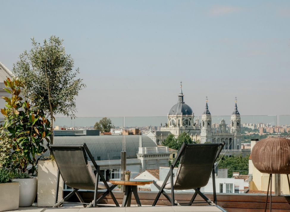 View of two lounge chairs on a rooftop looking over the spires and domes of Madrid.