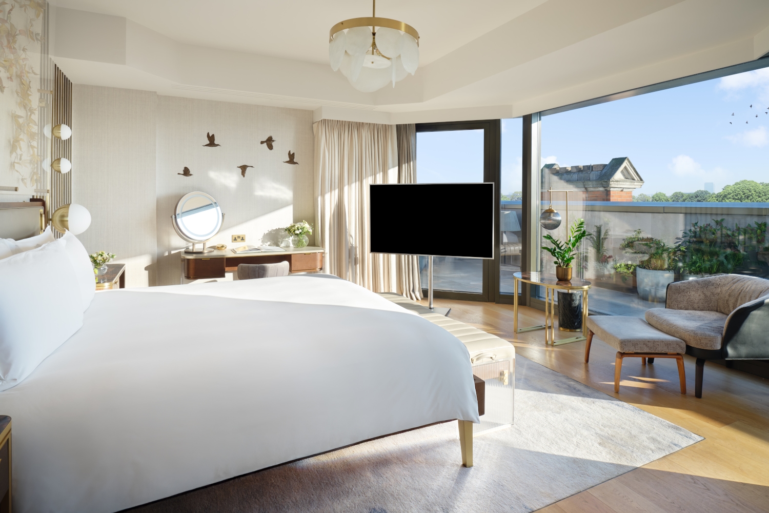 Interior of a bedroom with a white bed facing a large floor-to-ceiling window overlooking London.