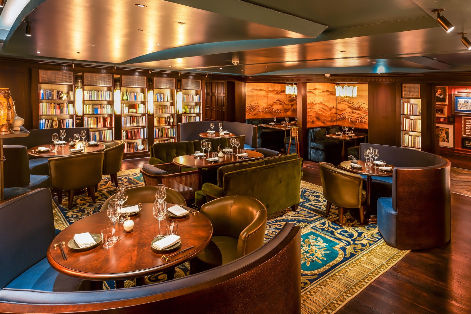 Interior of a dark wood bar with small tables in the foreground and a wooden bar in the background.