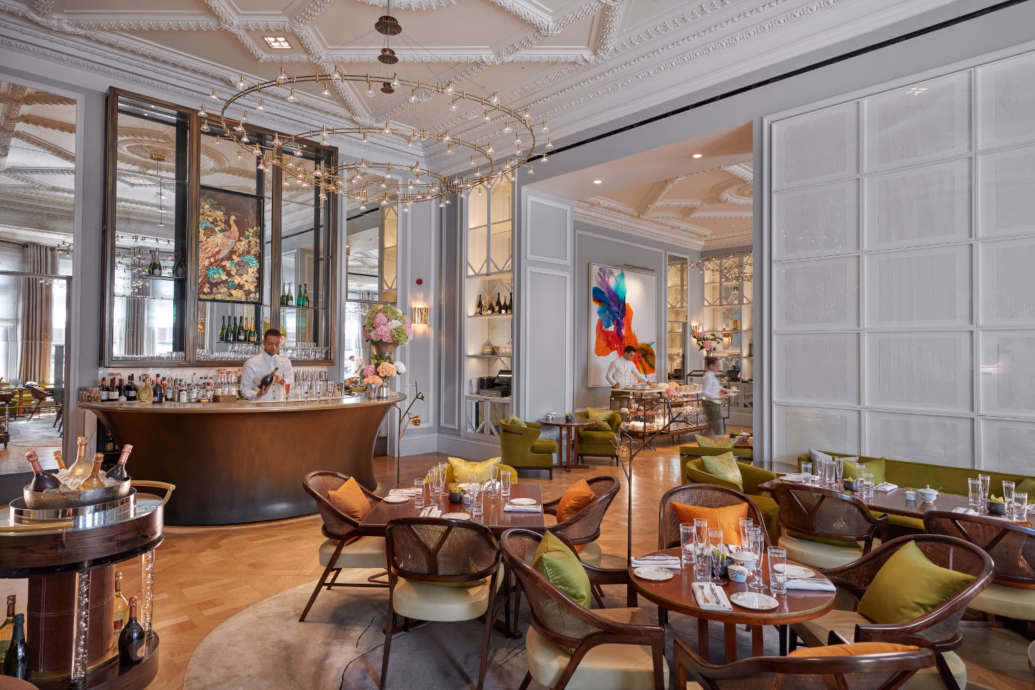 Interior of a grand reception cafe and bar with a few wooden tables and chairs and a small bar at the back in front of tall mirrors.