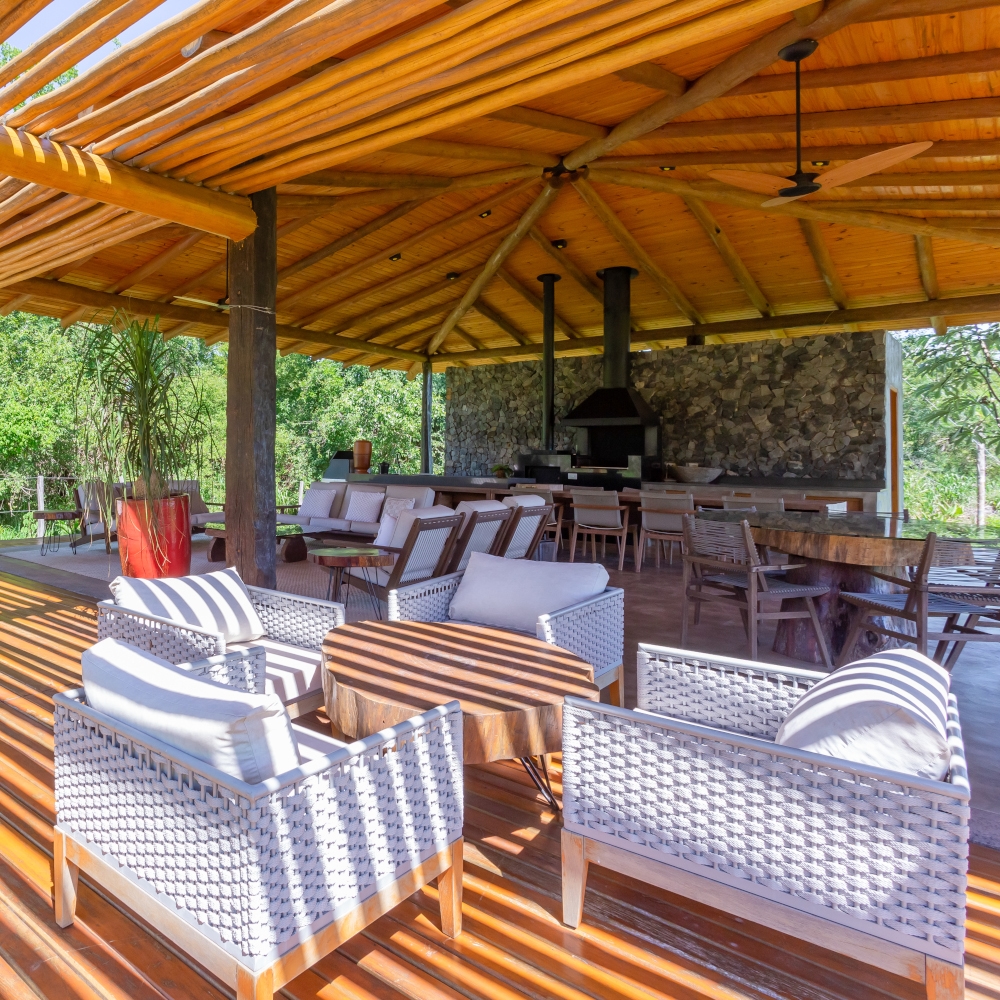 Covered open-air terrace with cushioned sofas and lounge chairs in the foreground and a large wood stove and pizza oven in the background.