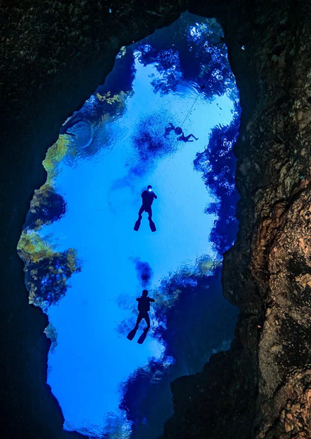 Overhead shot of divers swimming in a bright blue lake in a cave.