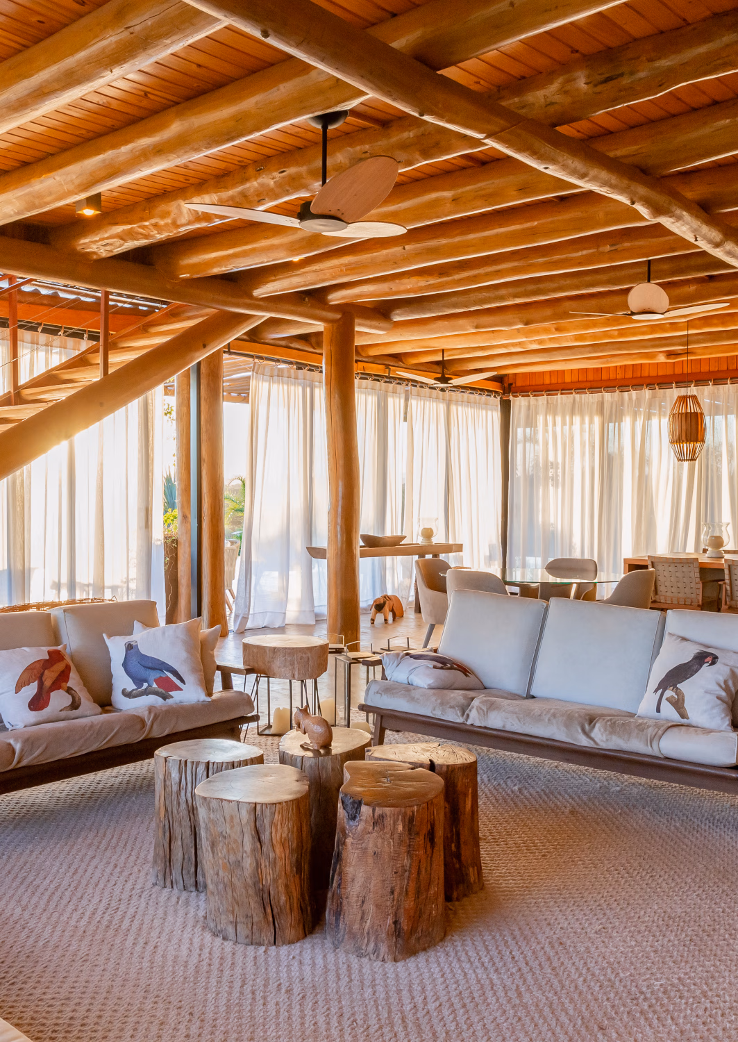 Interior of a villa living area with sofas and ceiling, stairs and pillars made of light wood.