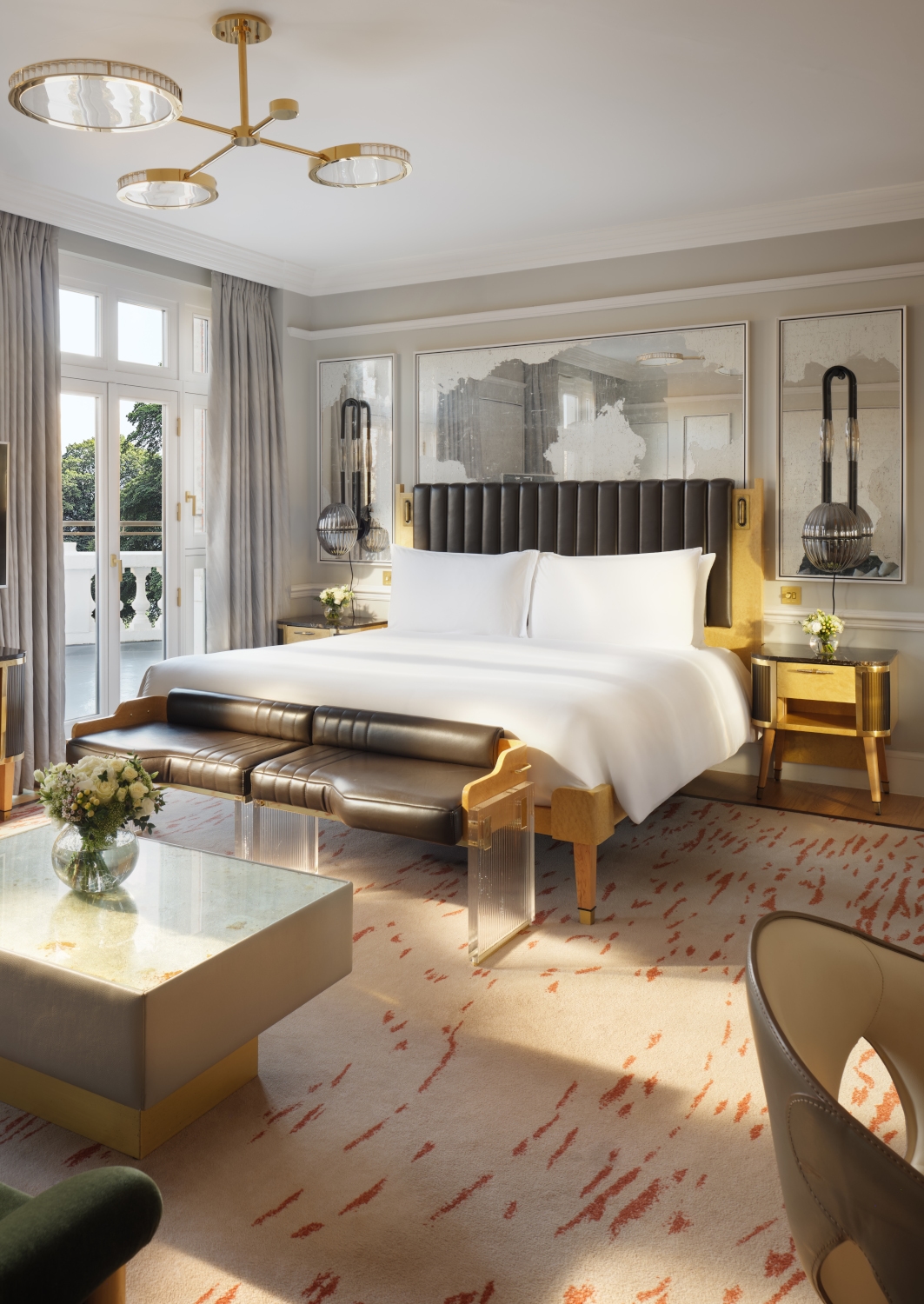 Interior of a bedroom with a white bed and dark grey headboard and a window opening out onto a juliette balcony with white railing.
