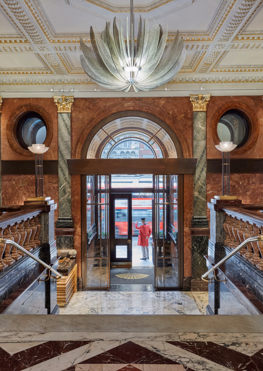 A grand entryway with marble walls and a staircase leading down to a door to the street.