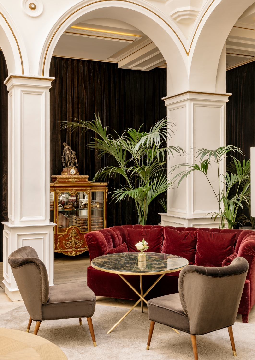 Interior of a reception area with arched pillarways, red plush sofas and ferns.