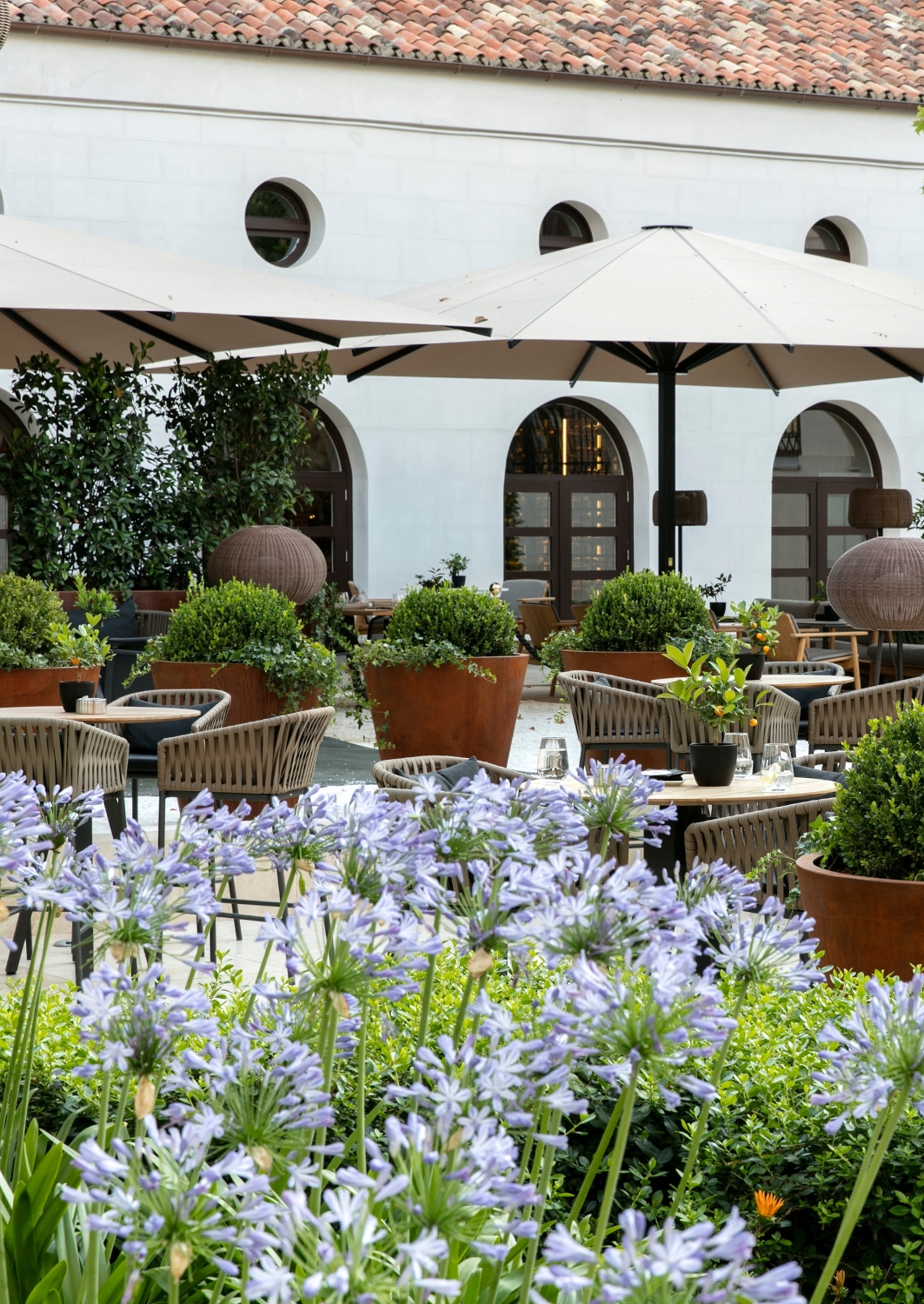 Exterior of courtyard seating area with several tables and chairs under large umbrellas.
