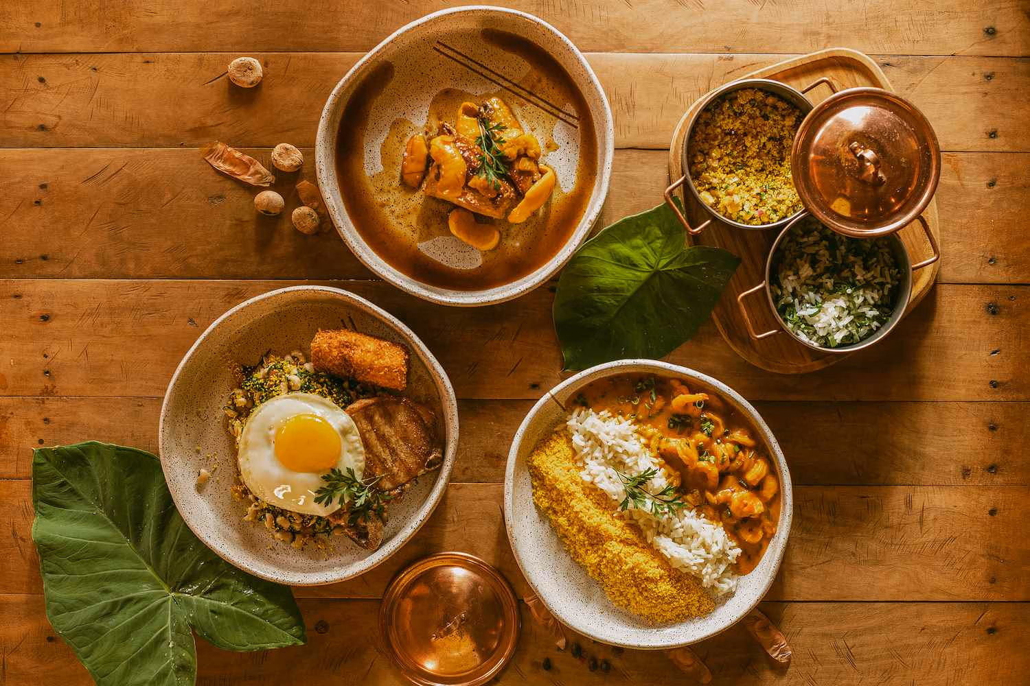 Three bowls with freshly prepared dishes including rice, prawns and a fried egg are laid out on a wooden table.