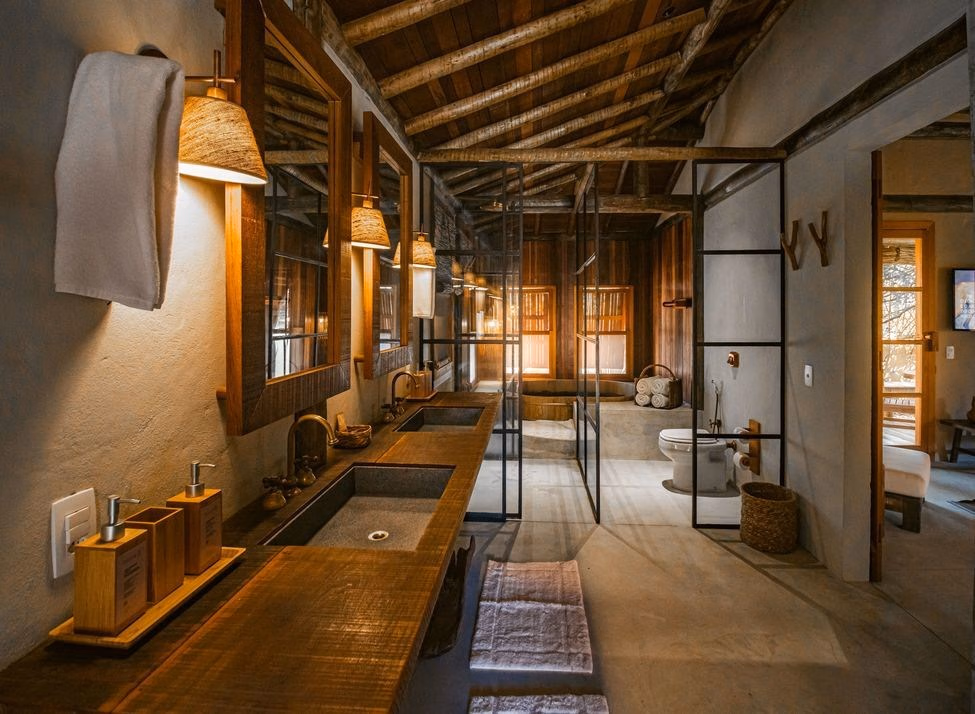 Luxury bathroom in muted shades with two sinks and glass doors leading to a toilet and hot tub, with entrance to master suite bedroom on the right